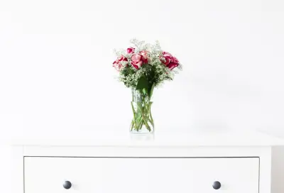 A small bouquet of roses in a glass vase on a white dresser
