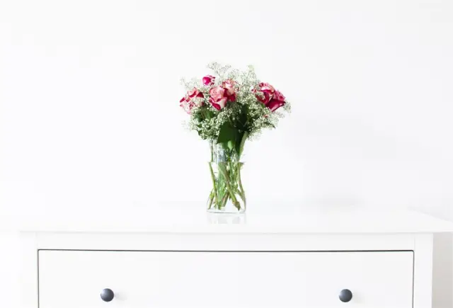 A small bouquet of roses in a glass vase on a white dresser
