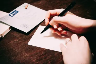 Hands writing a note on a white card next to an envelope on a wooden table