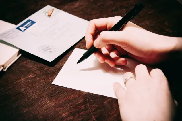 Hands writing a note on a white card next to an envelope on a wooden table