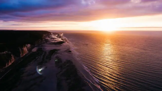 The sun setting over a calm sea below a line of cliffs