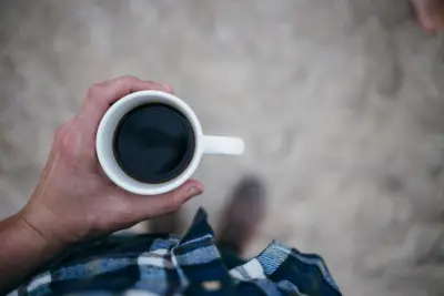 A hand holding a white cup of black coffee
