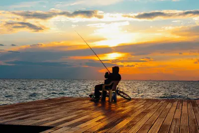The silhouette of a man fishing from a wooden dock at sunset over the water