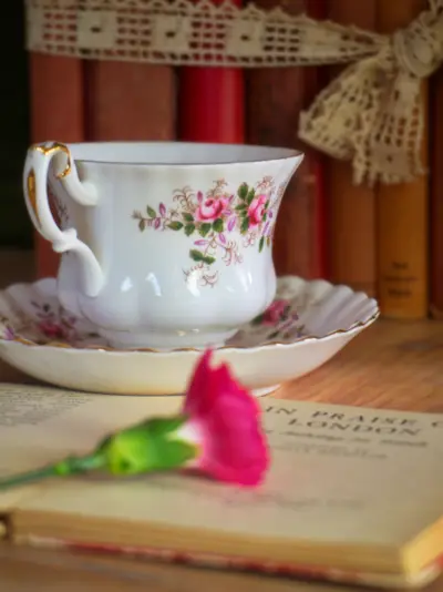 A flowered porcelain teacup on a stack of old books with a single pink rose