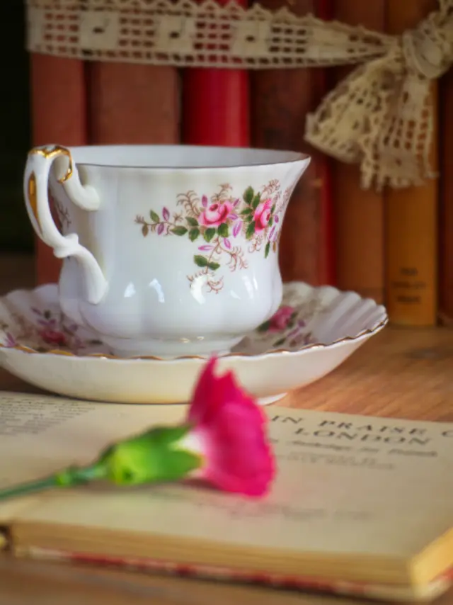 A flowered porcelain teacup on a stack of old books with a single pink rose